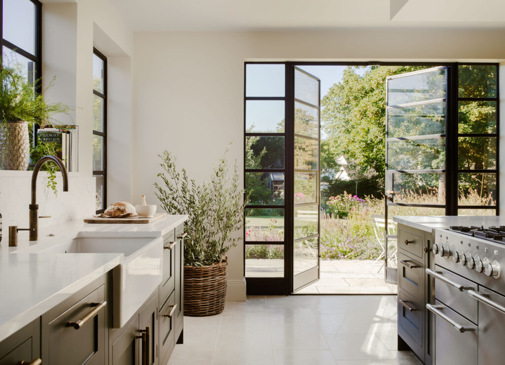 Dark green shaker kitchen with modern appliances, black crittall doors open onto a garden view.